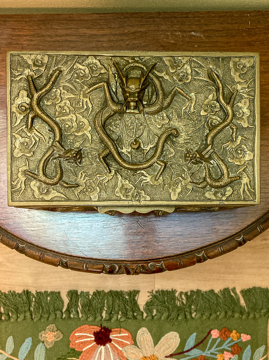 Decorative brass box with intricate designs on a wooden surface with floral rug. Antique Hand Engraved Sculptural Brass Dragon Wood Lined Cigar Box