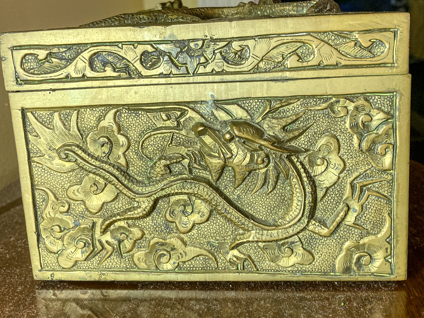 Decorative brass box with intricate dragon design on a reflective surfaceAntique Hand Engraved Sculptural Brass Dragon Wood Lined Cigar Box
