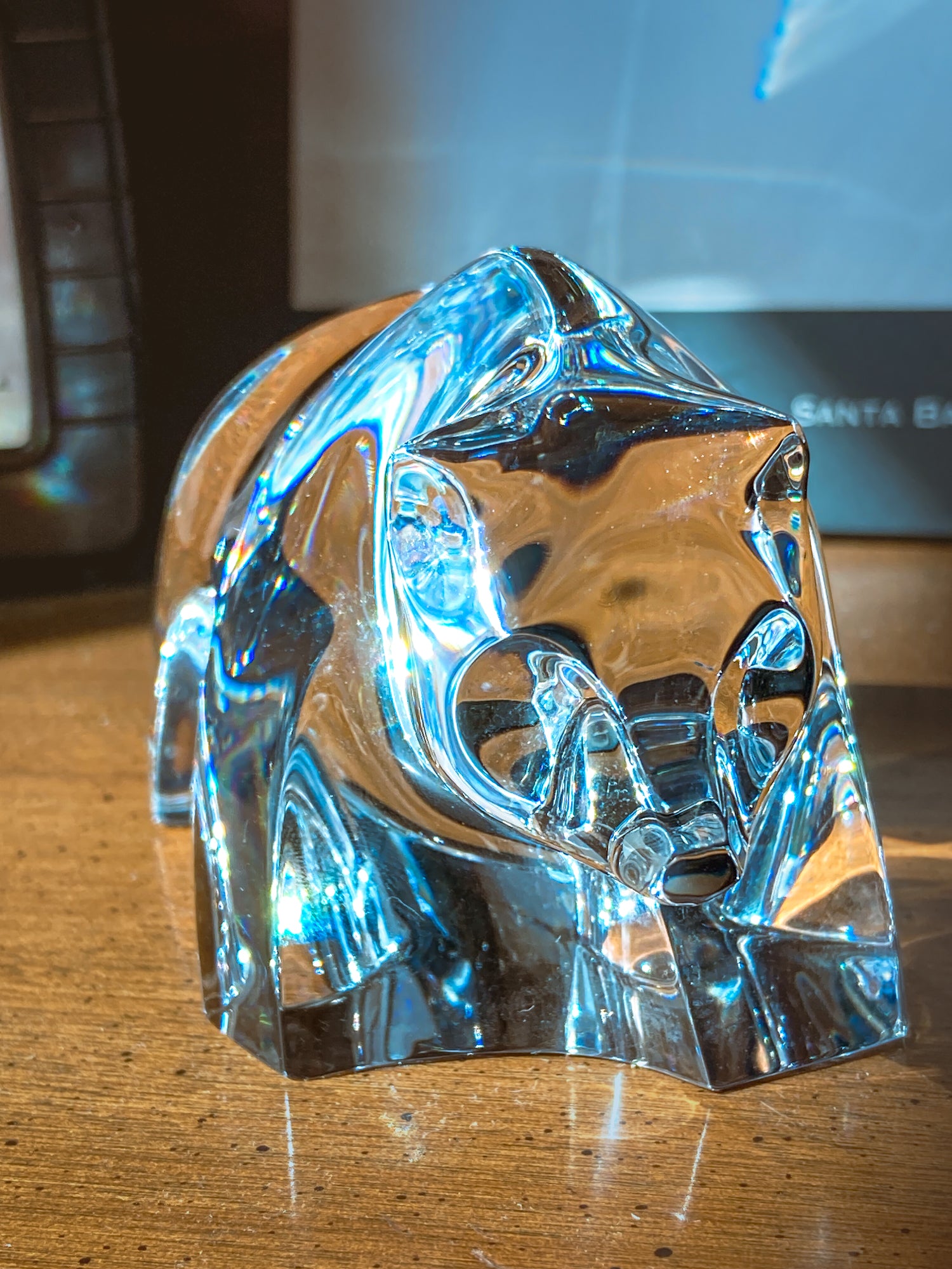 Crystal bear figurine on a wooden surface with camera and book in background. Baccarat Crystal Clear Oursons Wall Street Bear Paperweight Sculpture