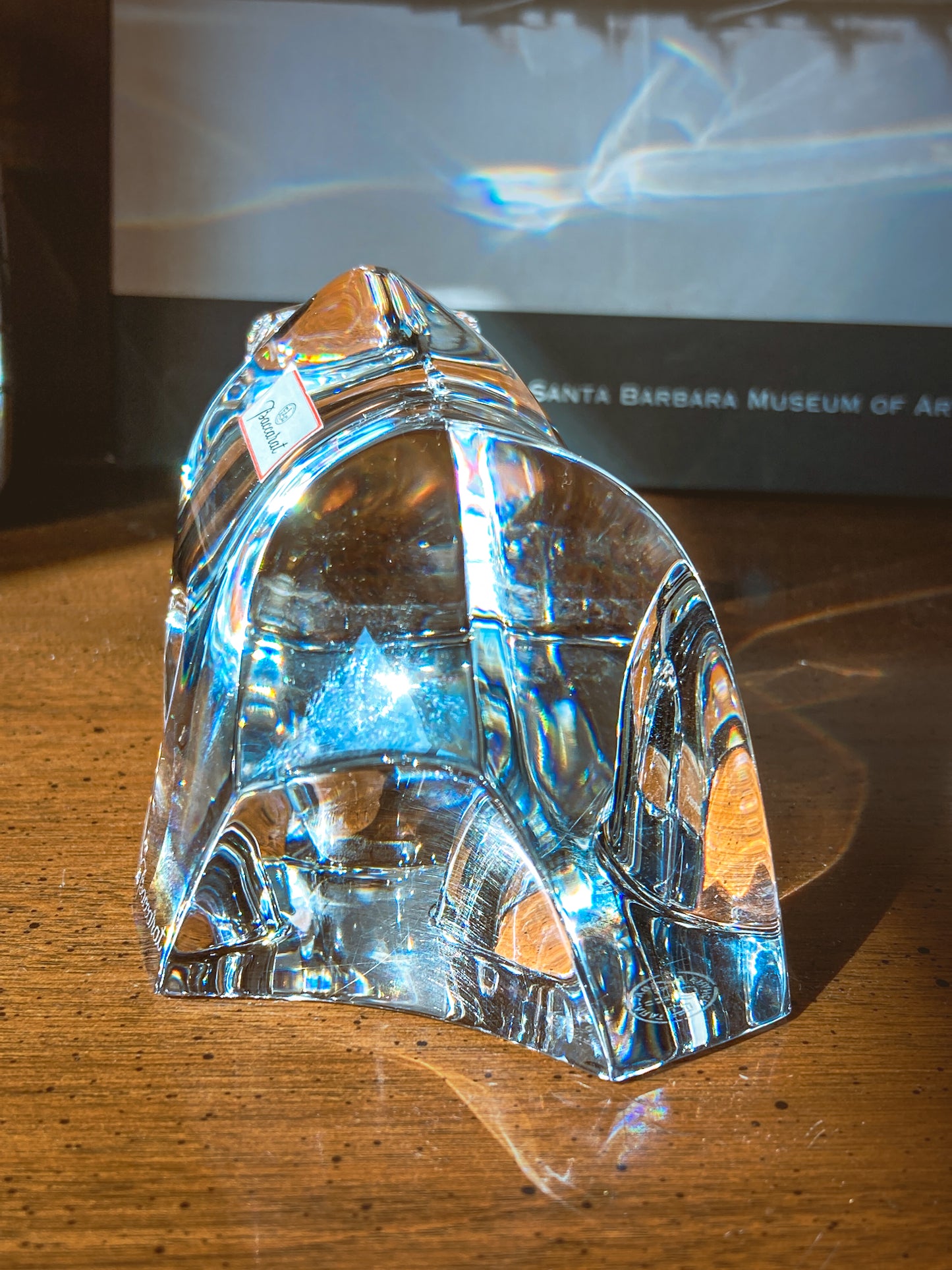 Crystal bear figurine on a wooden surface with camera and book in background. Baccarat Crystal Clear Oursons Wall Street Bear Paperweight Sculpture