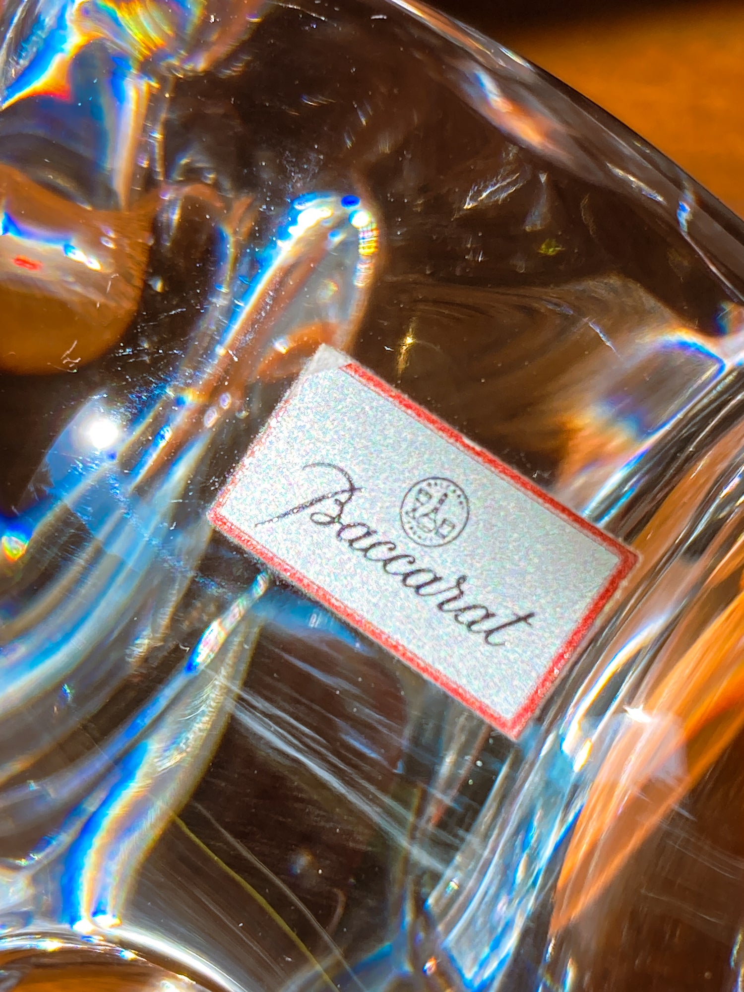 Close-up of a Baccarat crystal product with a visible label. Crystal bear figurine on a wooden surface with camera and book in background. Baccarat Crystal Clear Oursons Wall Street Bear Paperweight Sculpture