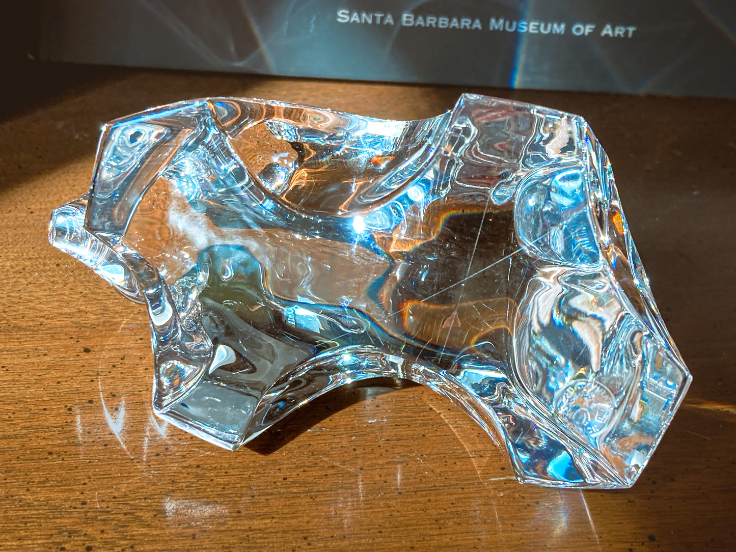 Clear glass sculpture on a wooden surface with 'Santa Barbara Museum of Art' book  in the background  Baccarat Crystal Clear Oursons Wall Street Bear Paperweight Sculpture