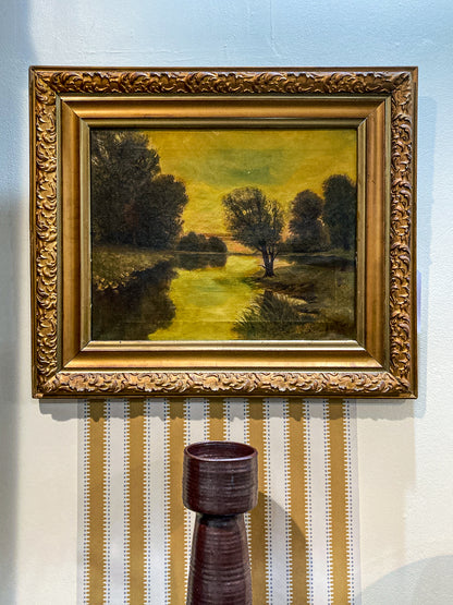 Framed painting of a landscape with trees and a river, displayed on a wall. Antique 1927 Serene River Landscape Framed Signed Oil Painting