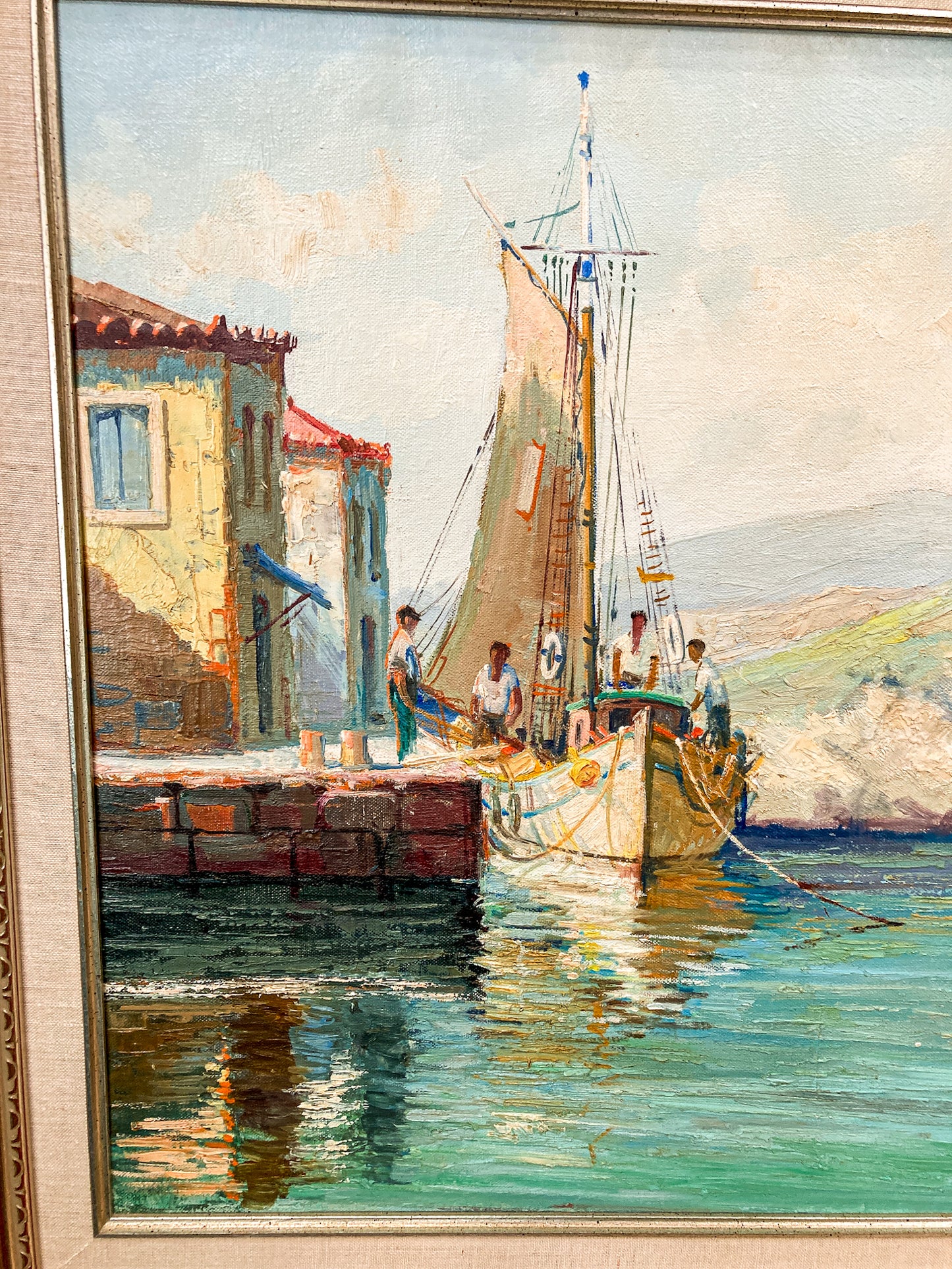 A framed painting depicting a coastal harbor scene with a sailboat moored beside a stone pier and colorful buildings, rendered in soft pastel and impressionistic brushwork. Vintage 1960s Greece Village Seaside Boat Dock Landscape Signed Framed Oil Painting