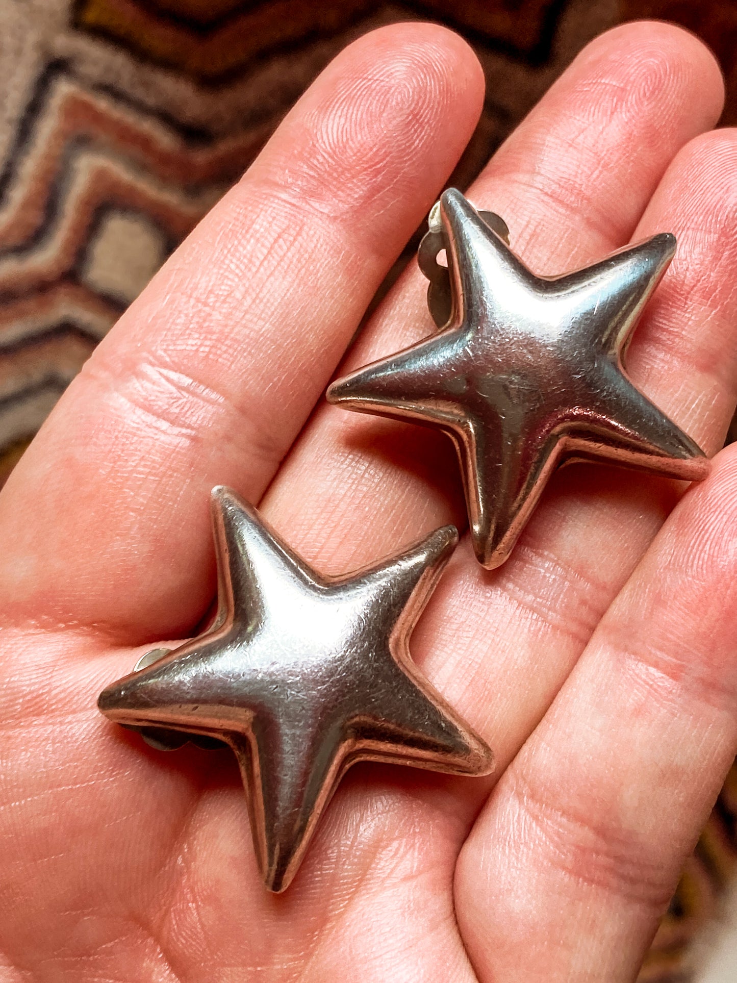 Two star-shaped Vintage 925 Sterling Silver Dimensional Bubble Star Clip On Earrings objects held in a hand with a patterned background