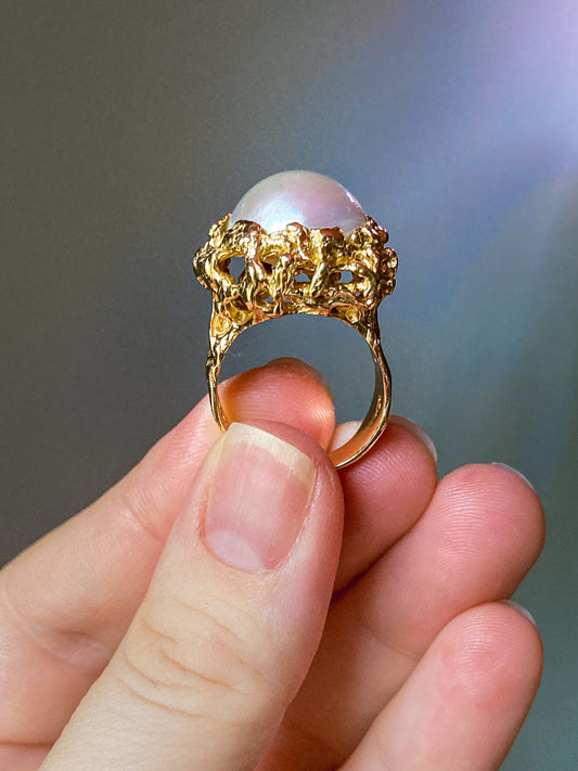 Gold ring with a pearl held between fingers against a blurred background. Vintage Artisan 14K Yellow Gold Pearl Organic Brutalist Cocktail Ring