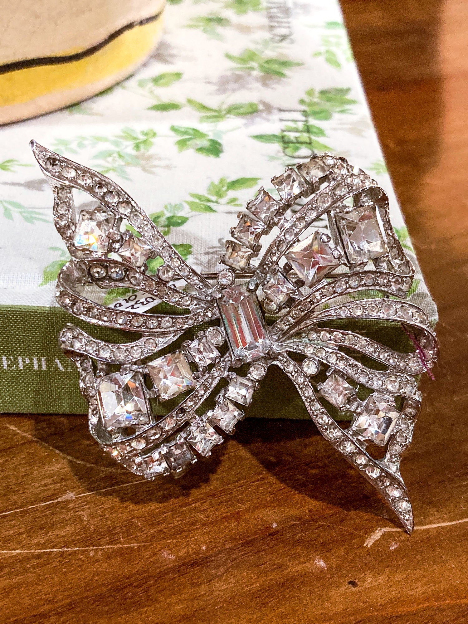 Vintage Coro Sterling Silver Clear Glass Rhinestone Asymmetric Bow Brooch Pin on floral book and wood table