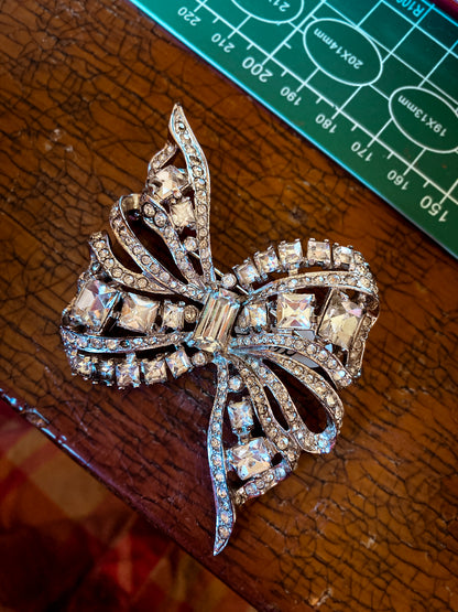 Vintage Coro Sterling Silver Clear Glass Rhinestone Asymmetric Bow Brooch Pin on a crackled wooden table
