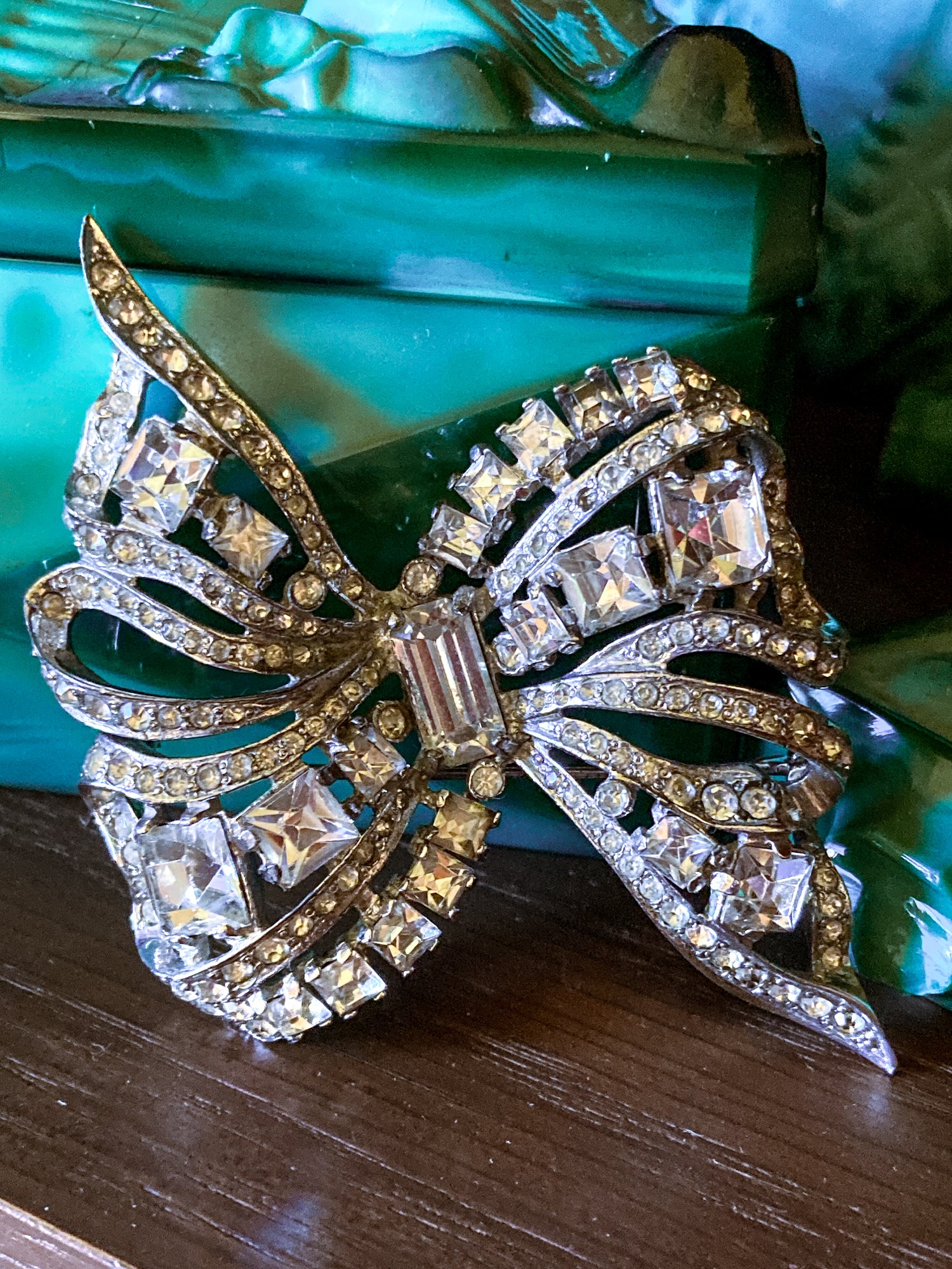 Vintage Coro Sterling Silver Clear Glass Rhinestone Asymmetric Bow Brooch Pin against green glass on wood surface