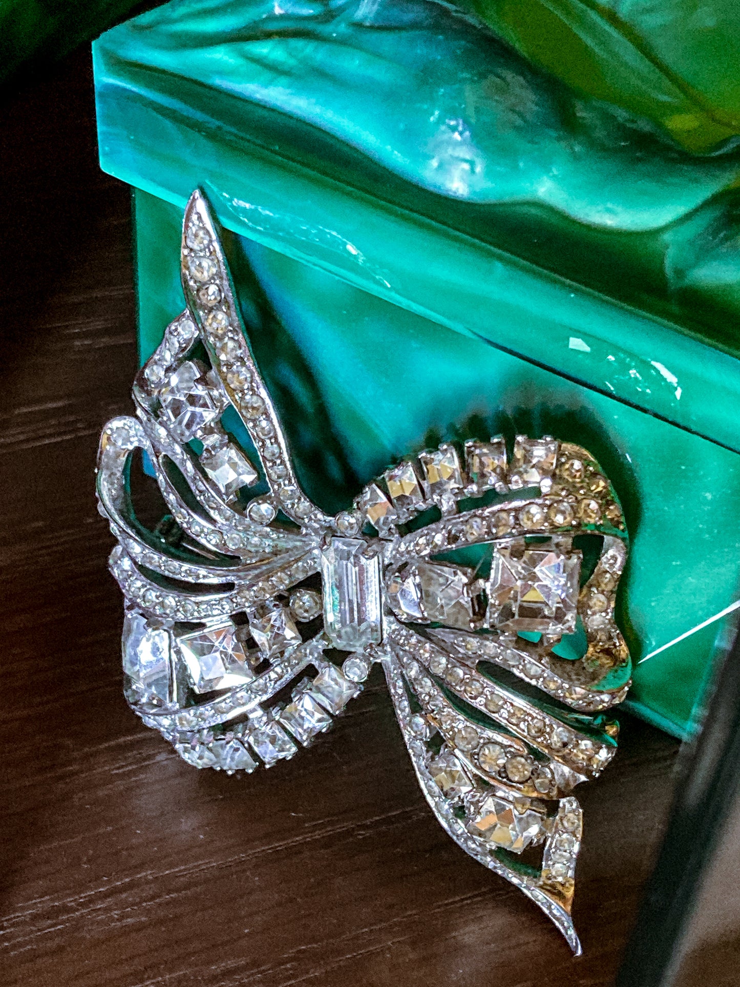 Vintage Coro Sterling Silver Clear Glass Rhinestone Asymmetric Bow Brooch Pin on green glass box and wood surface