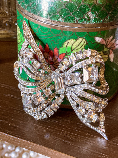 Vintage Coro Sterling Silver Clear Glass Rhinestone Asymmetric Bow Brooch Pin against green floral jar on wood surface