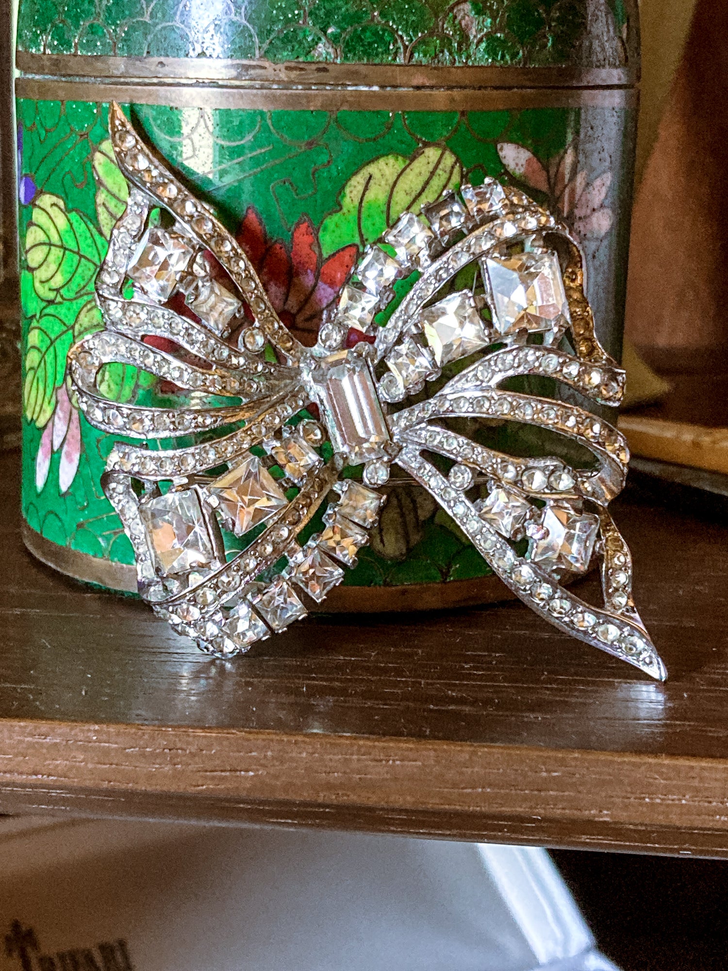 Vintage Coro Sterling Silver Clear Glass Rhinestone Asymmetric Bow Brooch Pin against green floral jar and wood surface