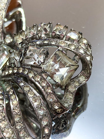 Vintage Coro Sterling Silver Clear Glass Rhinestone Asymmetric Bow Brooch Pin on mirrored white background close up