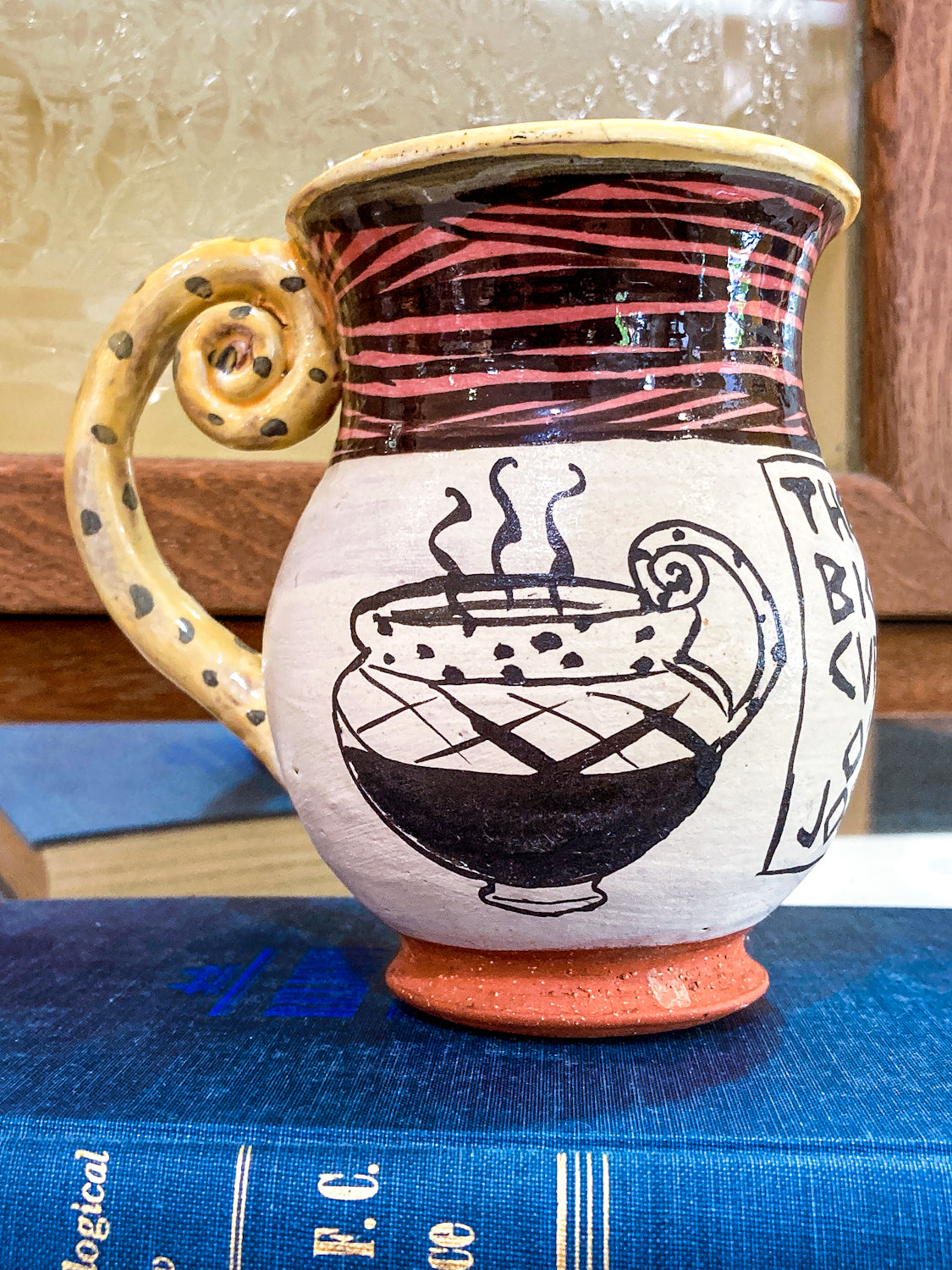 Handmade ceramic mug with artistic design on a blue book Vintage Daniel Postotnik Hand Potted Illustrative Portrait Mug As Found