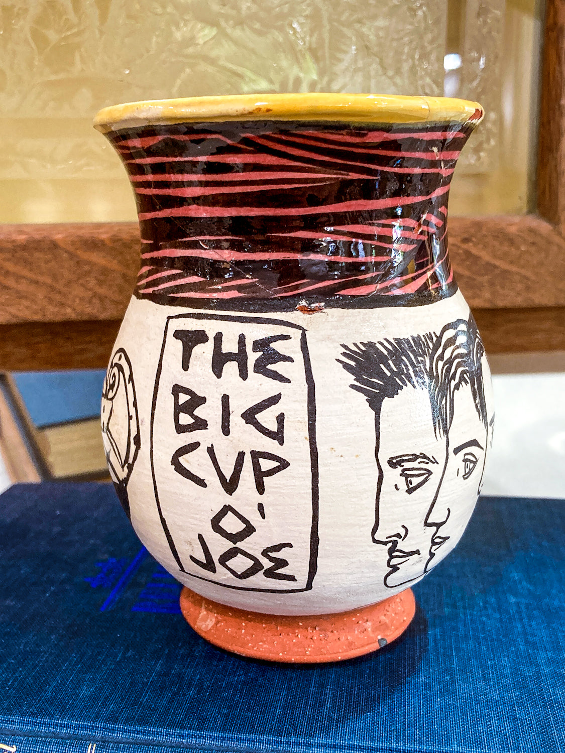 Decorative ceramic vase with artistic designs and text on a blue surface. Vintage Daniel Postotnik Hand Potted Illustrative Portrait Mug As Found
