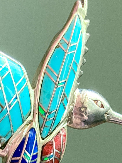 Close-up of a Vintage Sterling Silver Turquoise Gemstone Mosaic Inlay Hummingbird Brooch with colorful wings on a green background