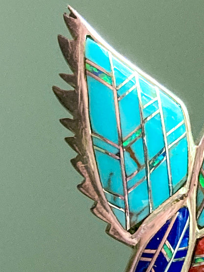 Close-up of a Vintage Sterling Silver Turquoise Gemstone Mosaic Inlay Hummingbird Broochjewelry piece with turquoise and silver design on a green background